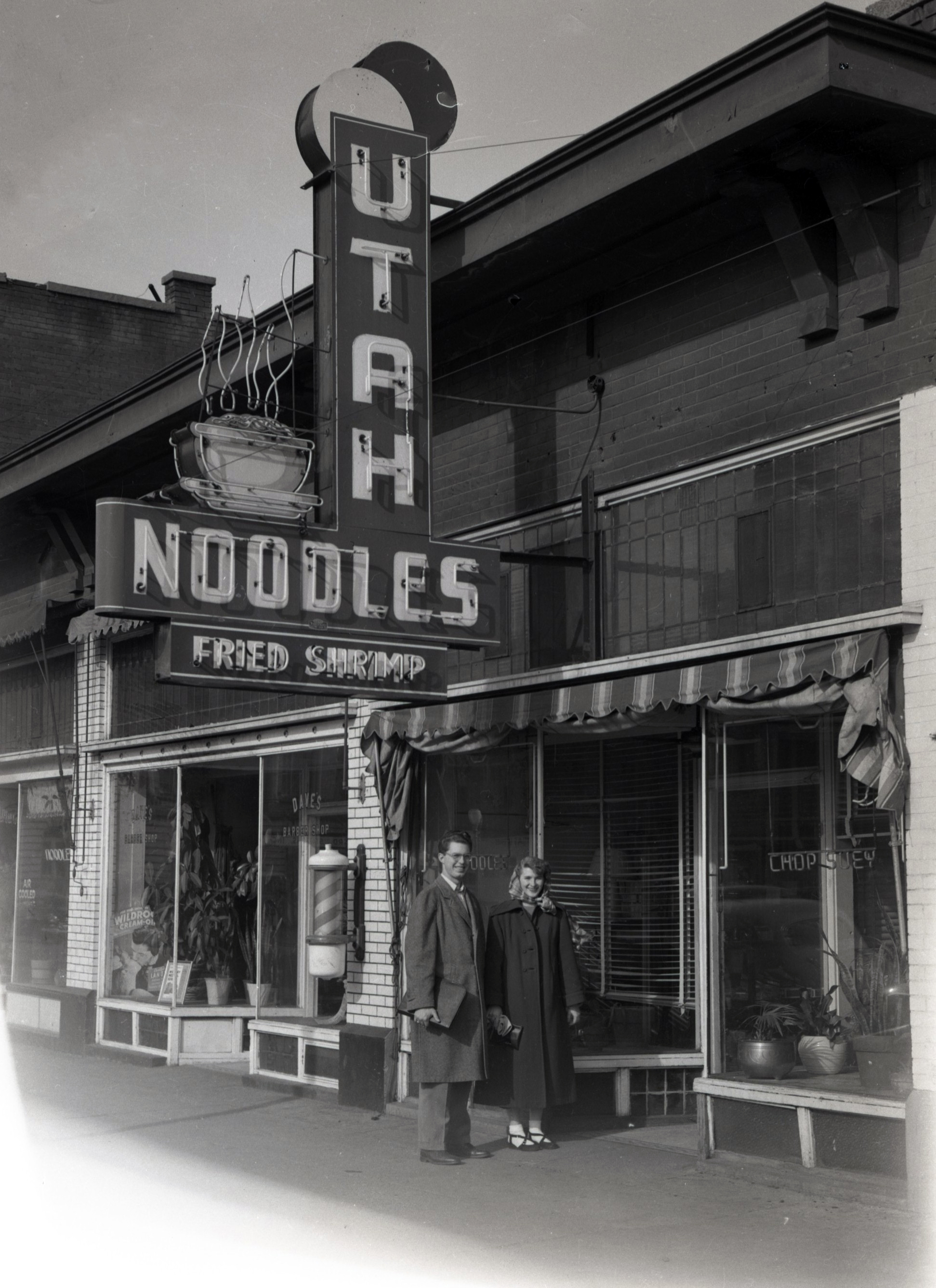 A couple posing under the neon sign of the Utah Noodle Parlor owned by Leo and Mamiyo Iseki at 2430 Grant Ave
