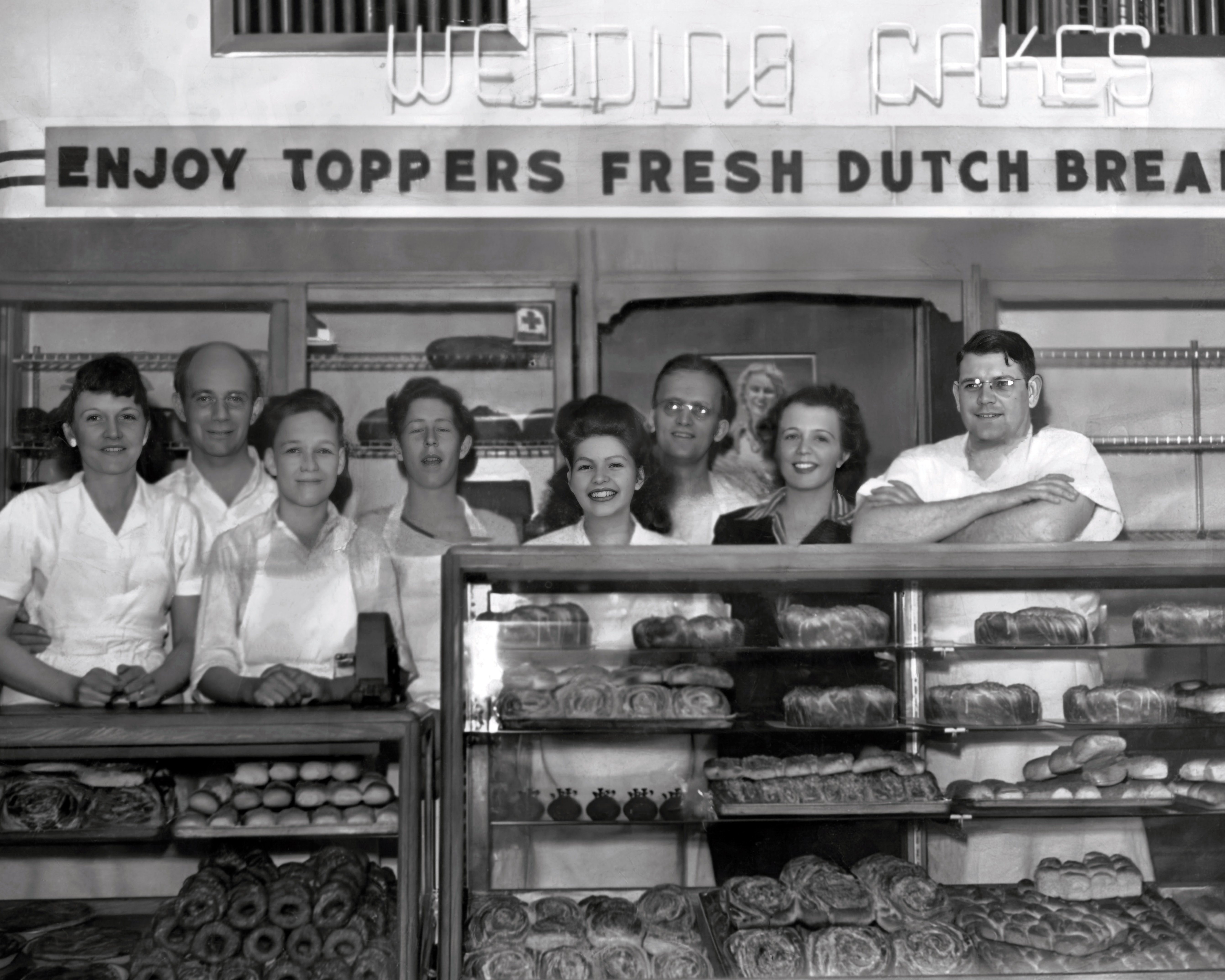 DeRyke family inside Topper Bakery standing behind a bakery case full of pastries.